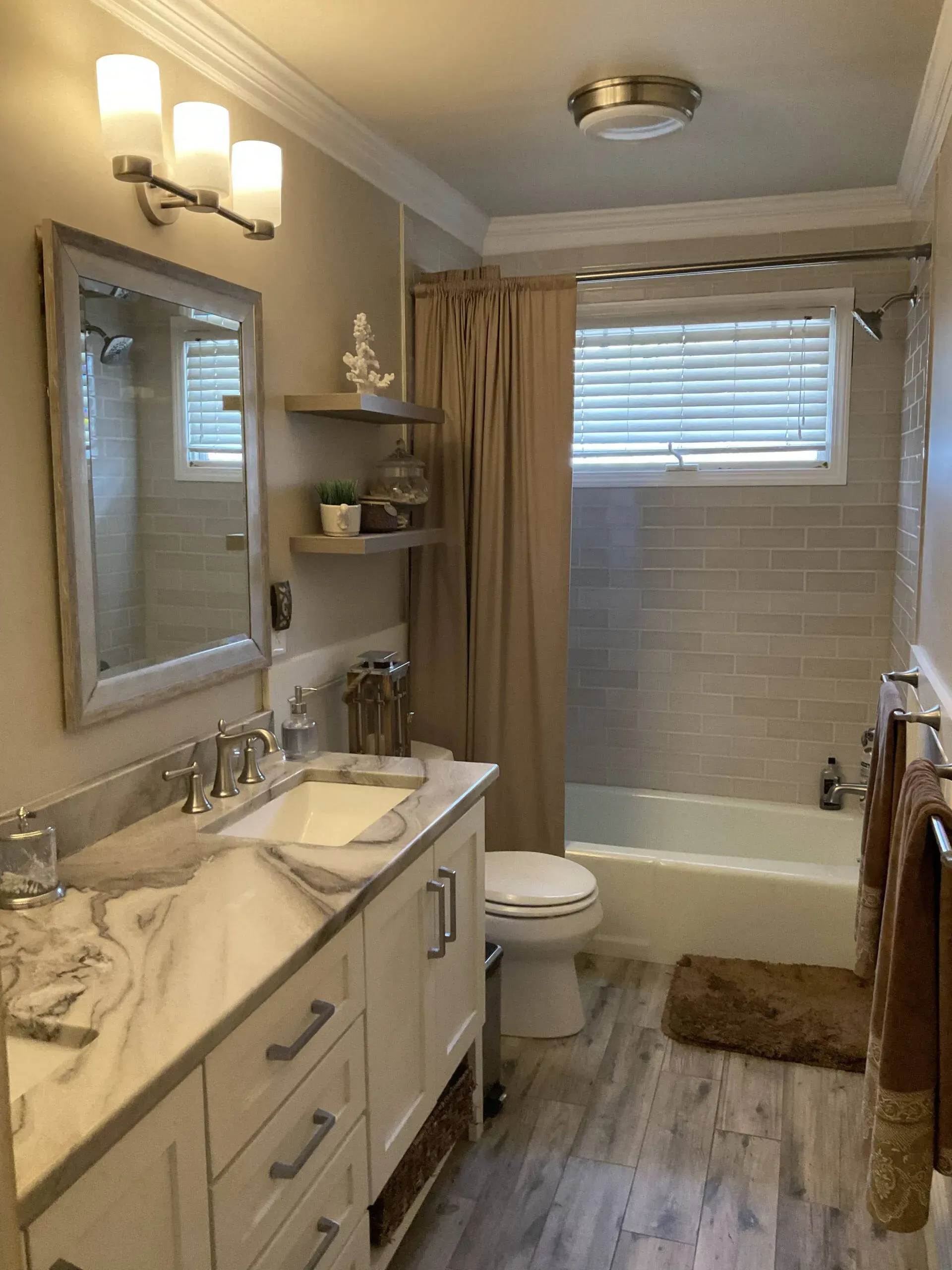 Small bathroom with double vanity, mirror, toilet, bathtub, beige walls, and window blinds