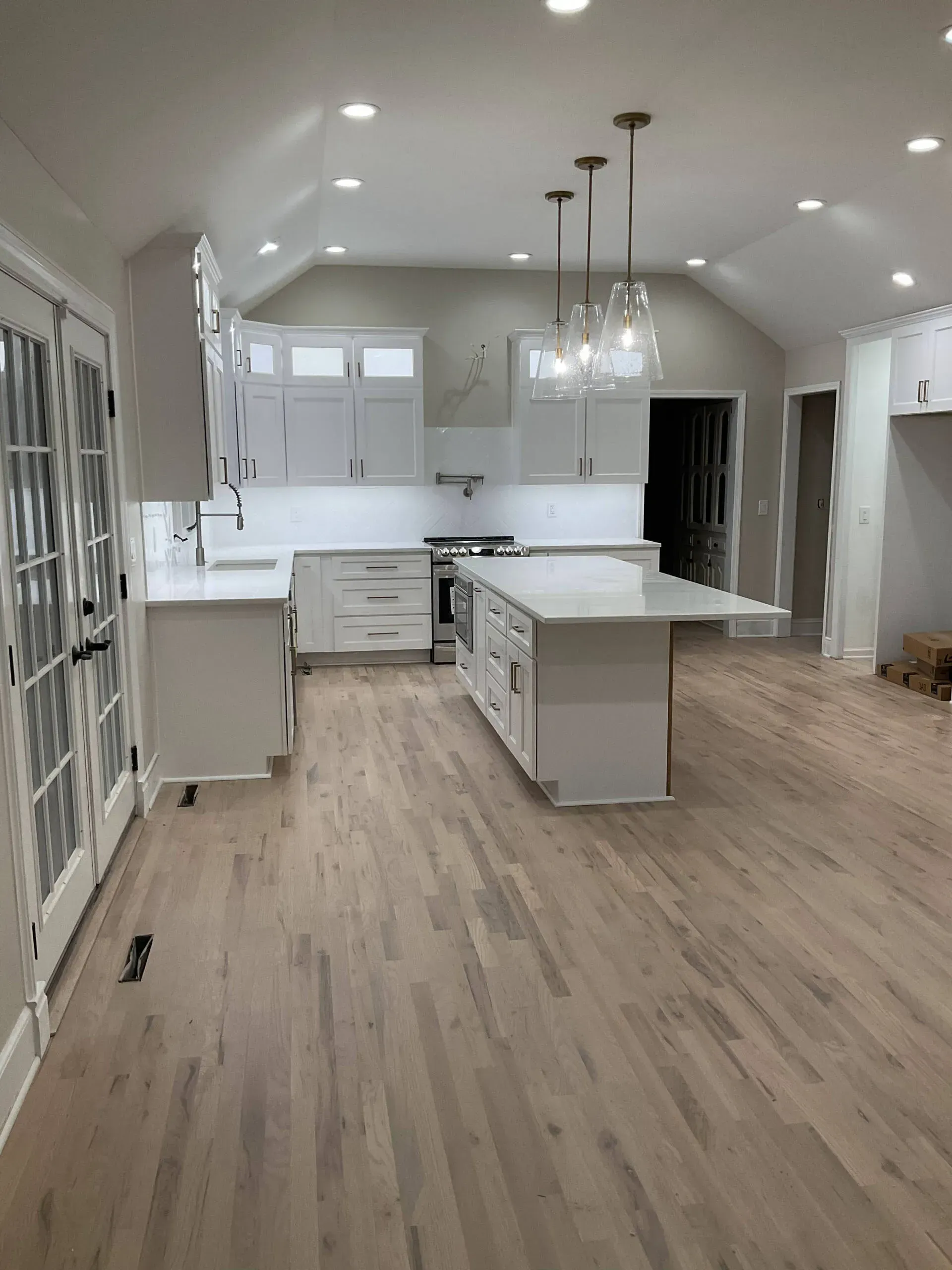 Bright modern kitchen with white cabinets, island, pendant lights, and wood floors