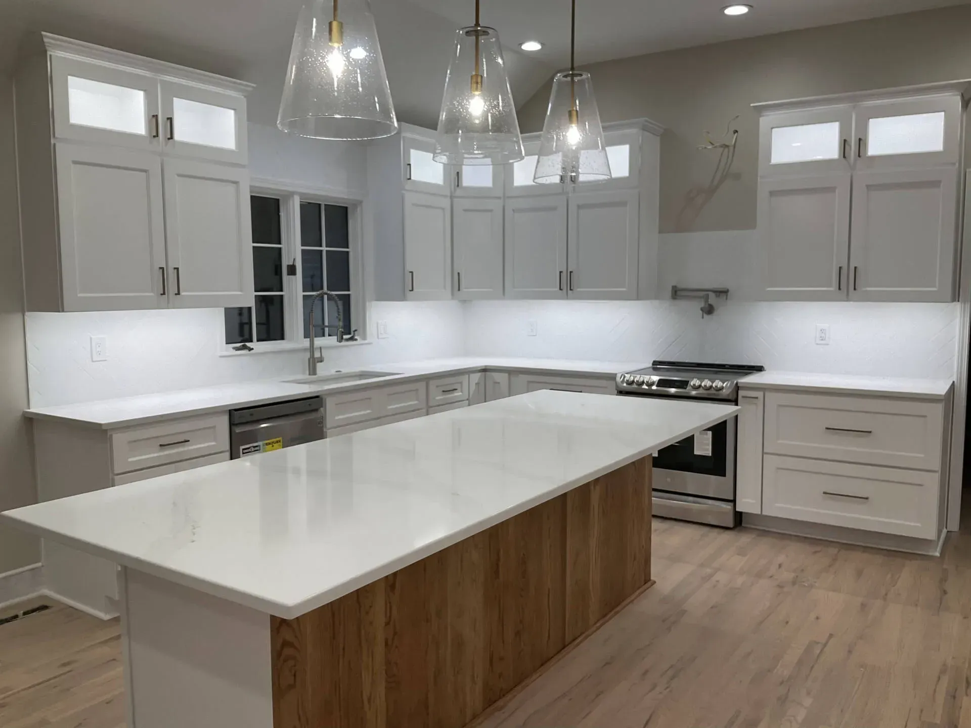 Bright modern kitchen with white cabinets, large island, pendant lights, and wood floors