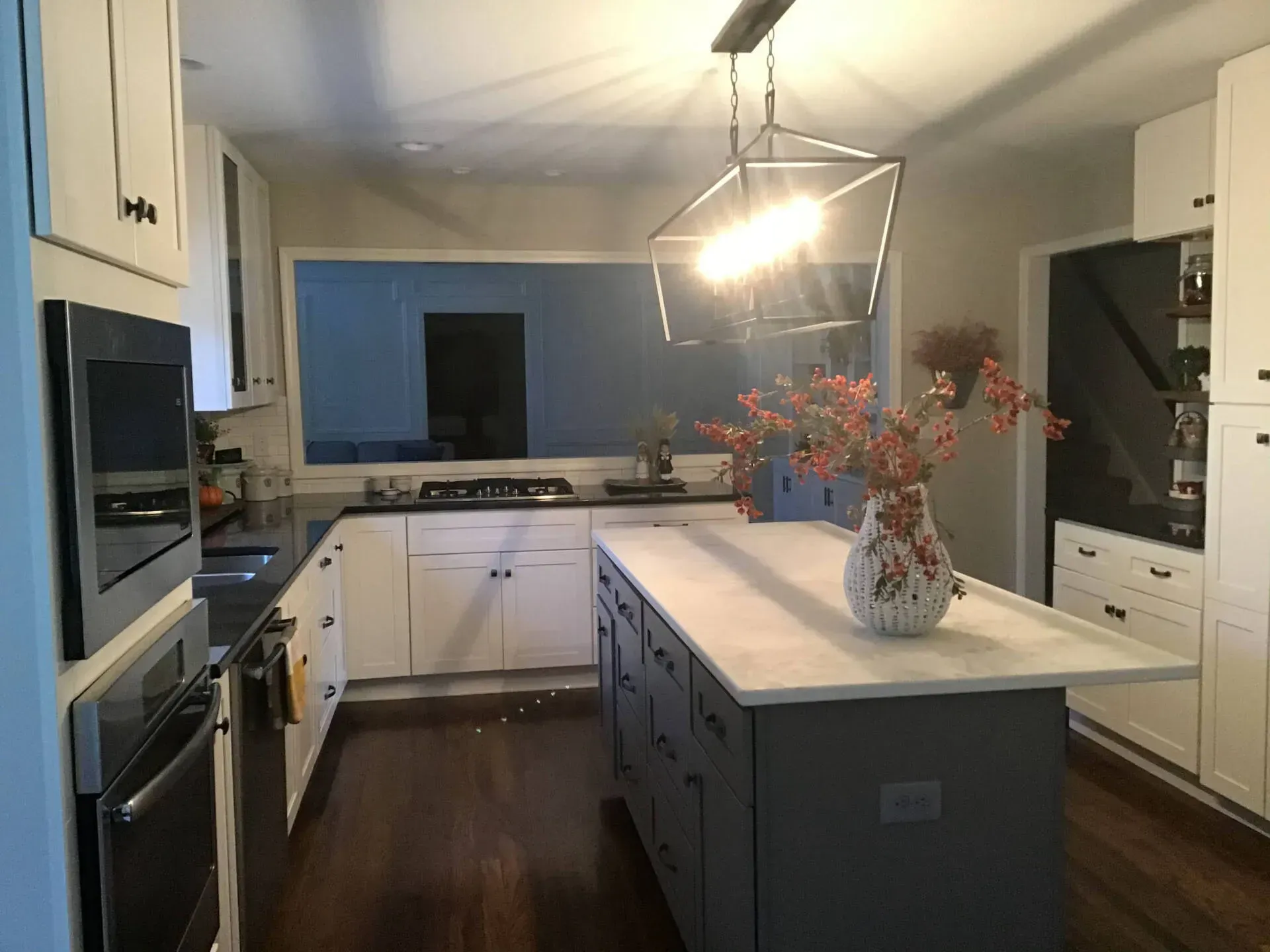 Bright modern kitchen with white cabinets, dark island, and vase of flowers under pendant lights