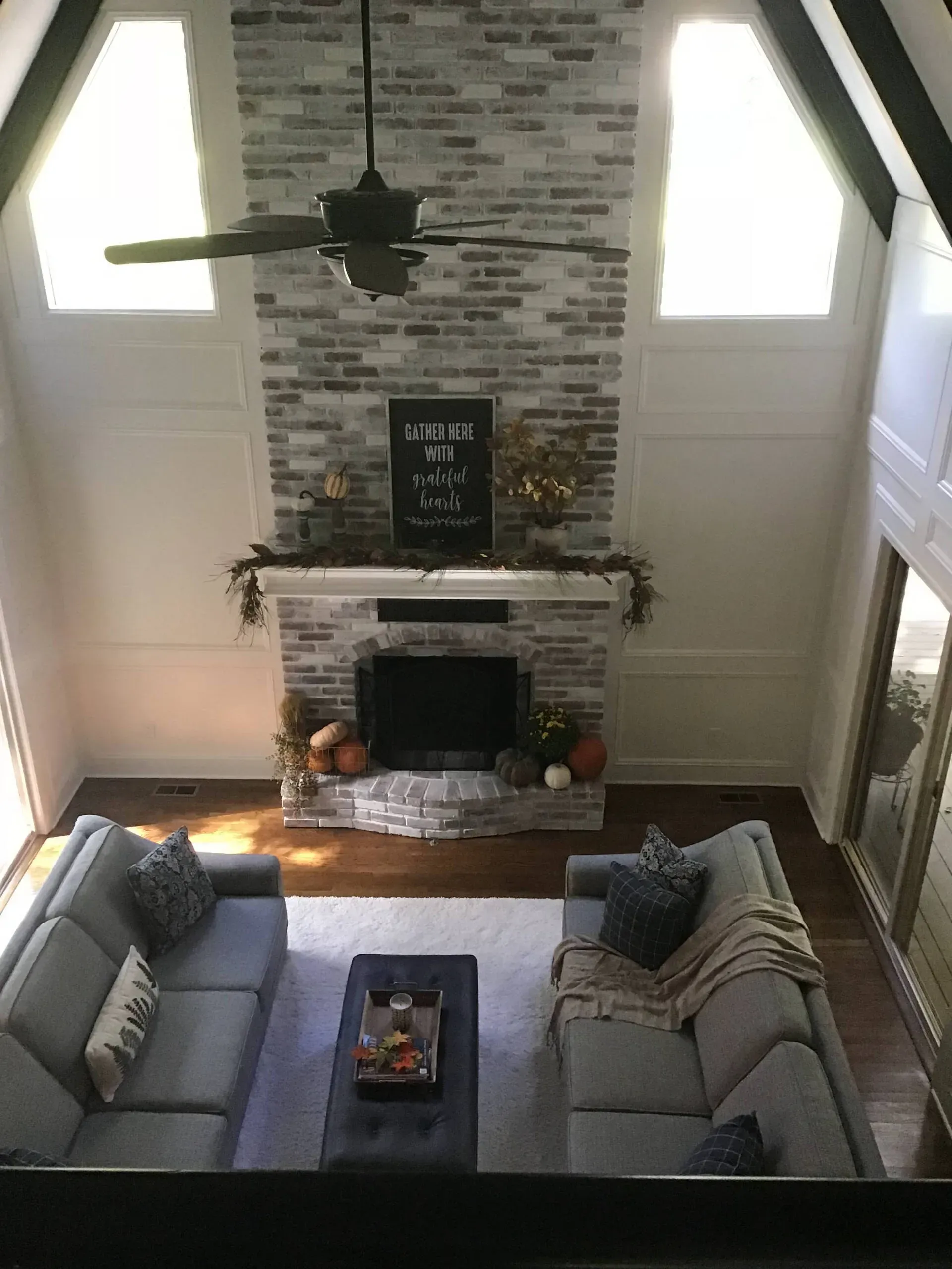 Living room with a fireplace, high ceiling, gray sofas, and a ceiling fan above a central coffee table