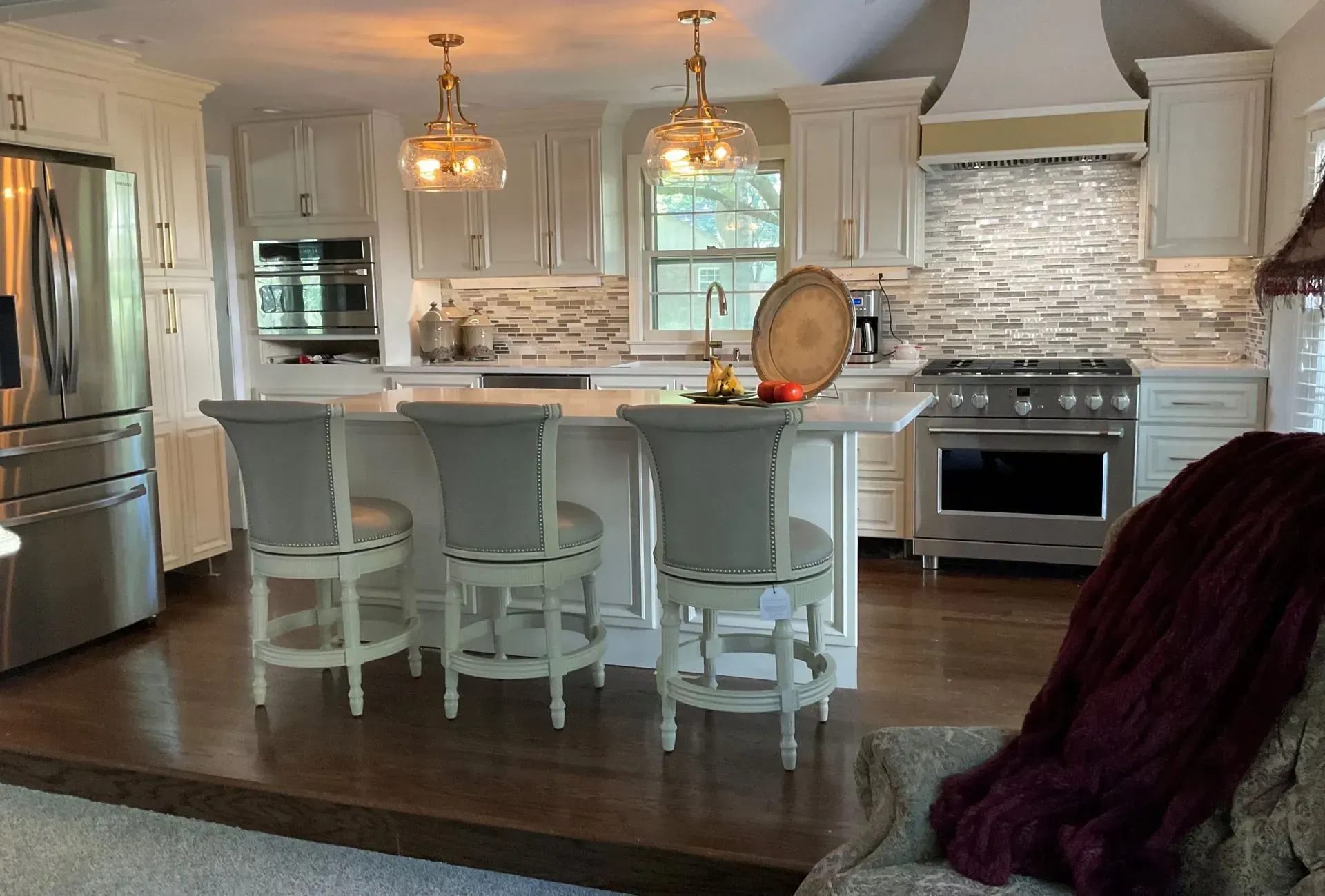 Bright kitchen with white cabinets, marble island, pendant lights, and stainless steel appliances