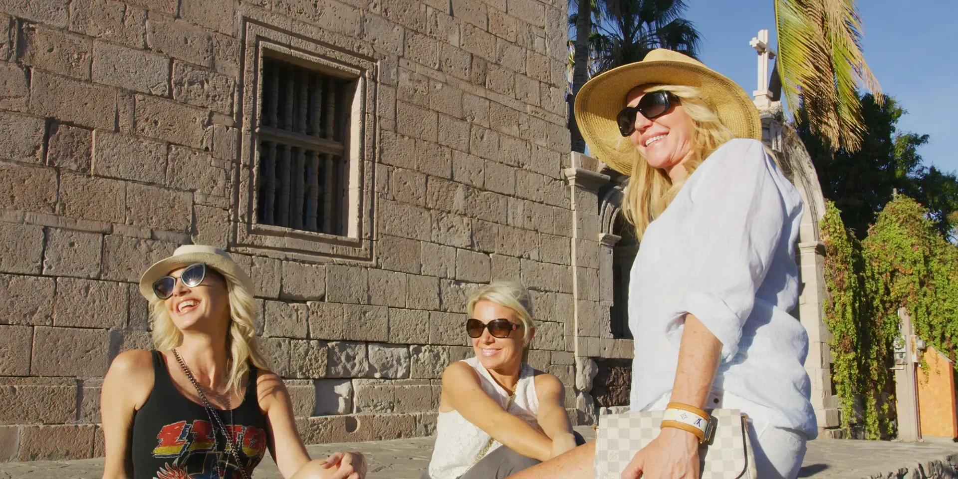 three women from danzante bya wearing hats and sunglasses are standing in front of a stone building in loreto, mexico