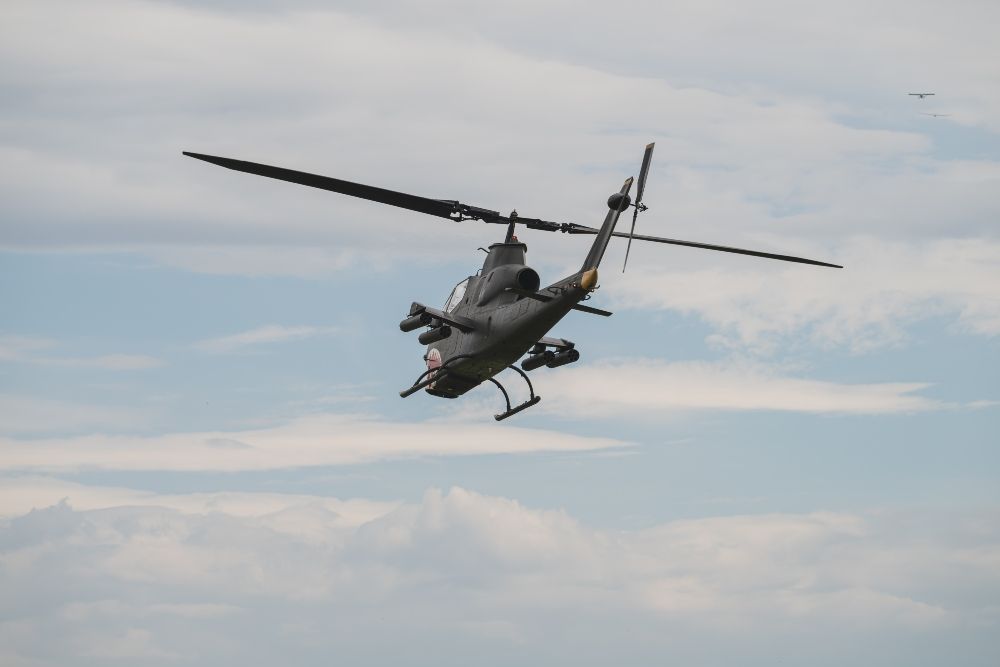 A military helicopter is flying through a cloudy sky.