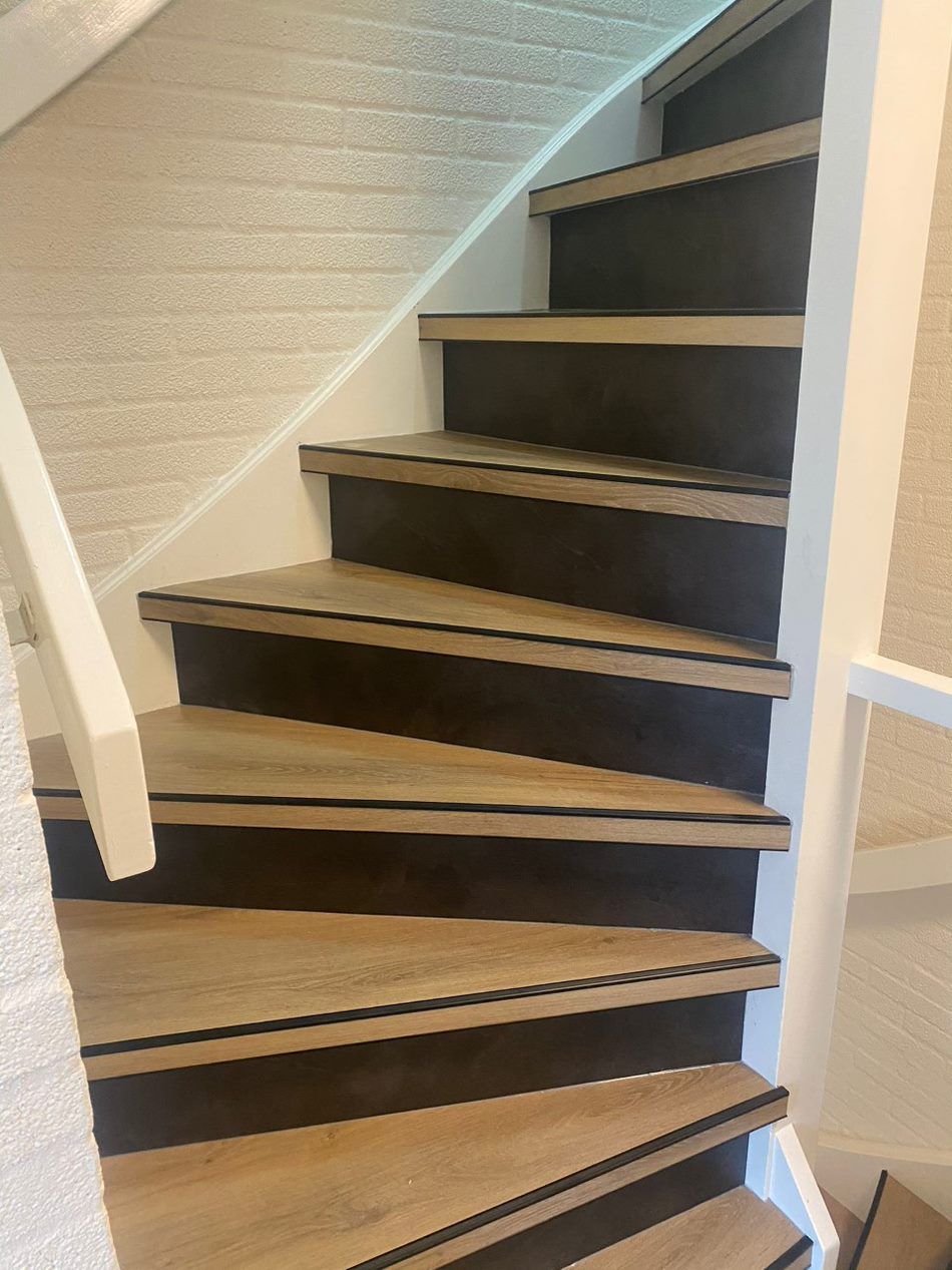 Een close-up van een houten trap met zwarte treden en een witte leuning.