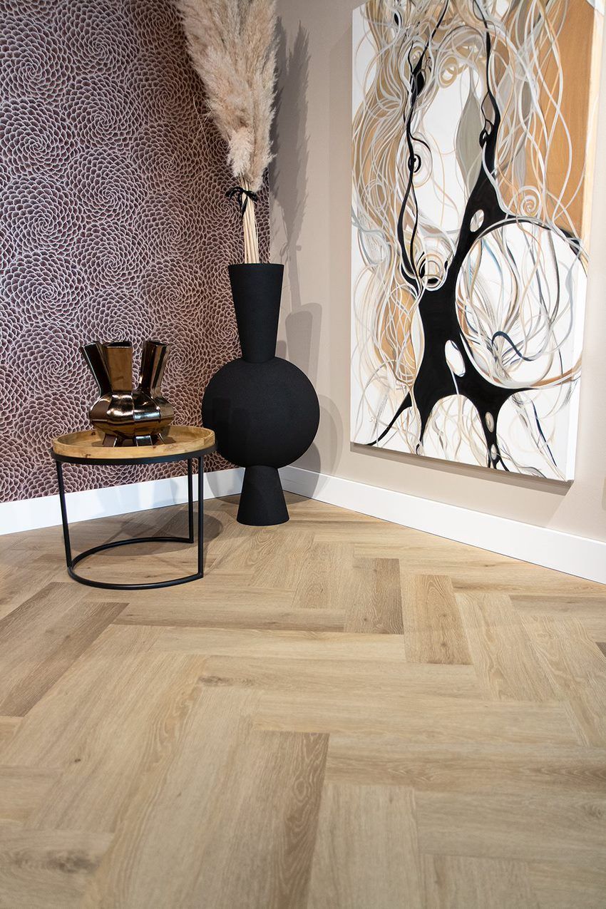 Een kamer met een houten vloer, een tafel, een vaas en een schilderij aan de muur.