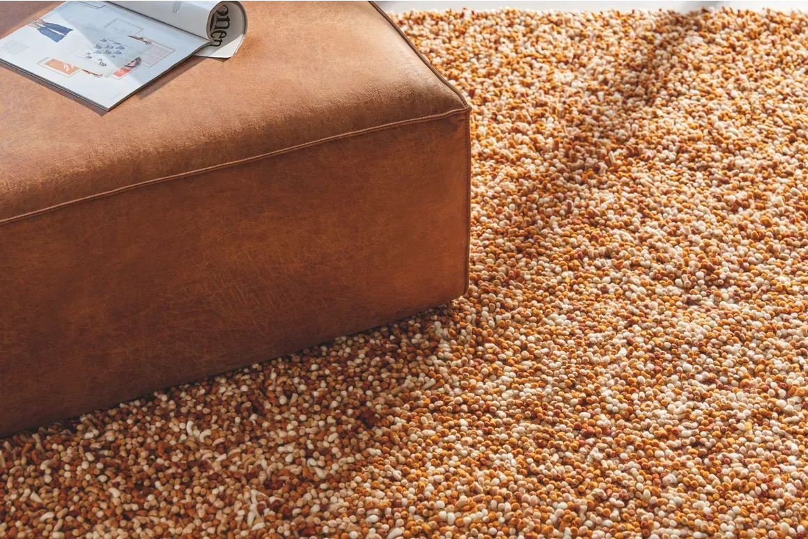 Een bruine poef staat op een kleed naast een tijdschrift