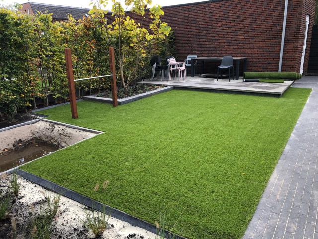 Een weelderig groen gazon in een achtertuin met een bakstenen gebouw op de achtergrond.