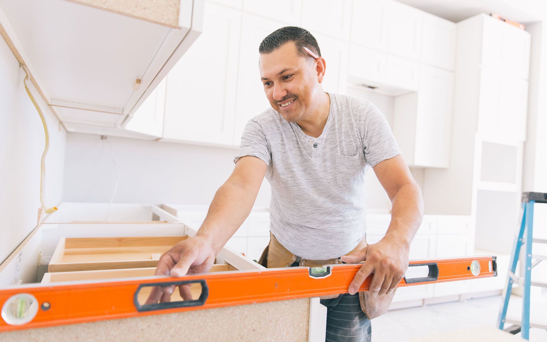 A man is using a level to measure a piece of wood in a kitchen.