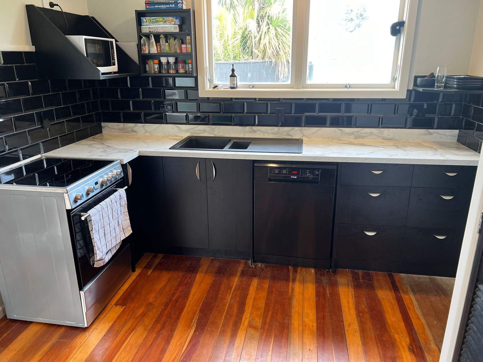 A kitchen with black cabinets , a stove , a sink , and a window.