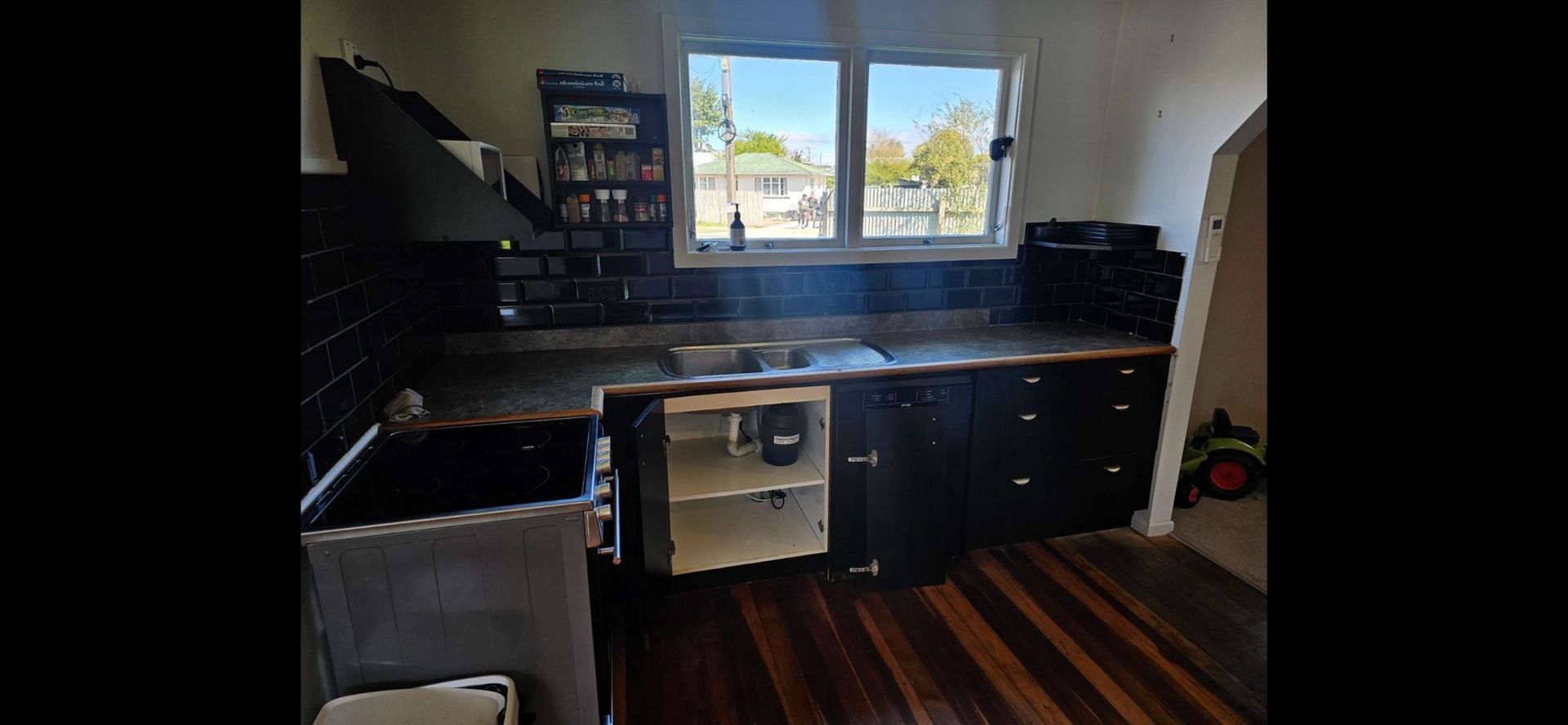 A kitchen with black cabinets , a stove , a sink , and a window.