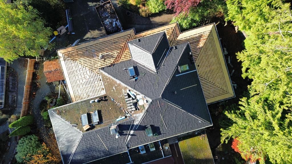 An aerial view of a house with a roof under construction surrounded by trees.