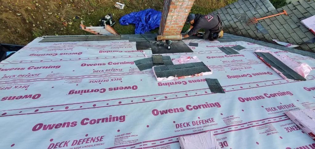 A man is working on a roof with a roofing material.