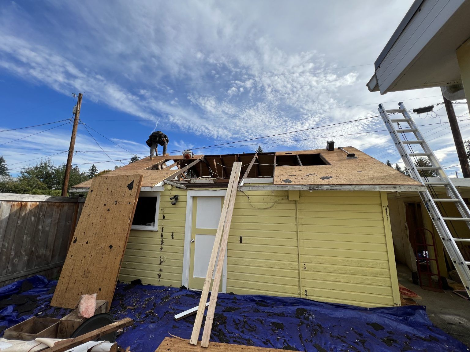 A yellow house is being remodeled with a ladder on the roof.