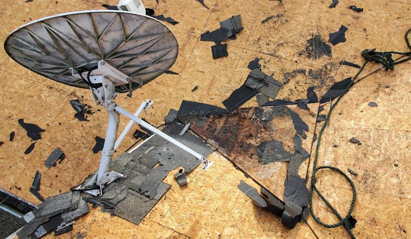 A satellite dish is sitting on top of a broken roof.