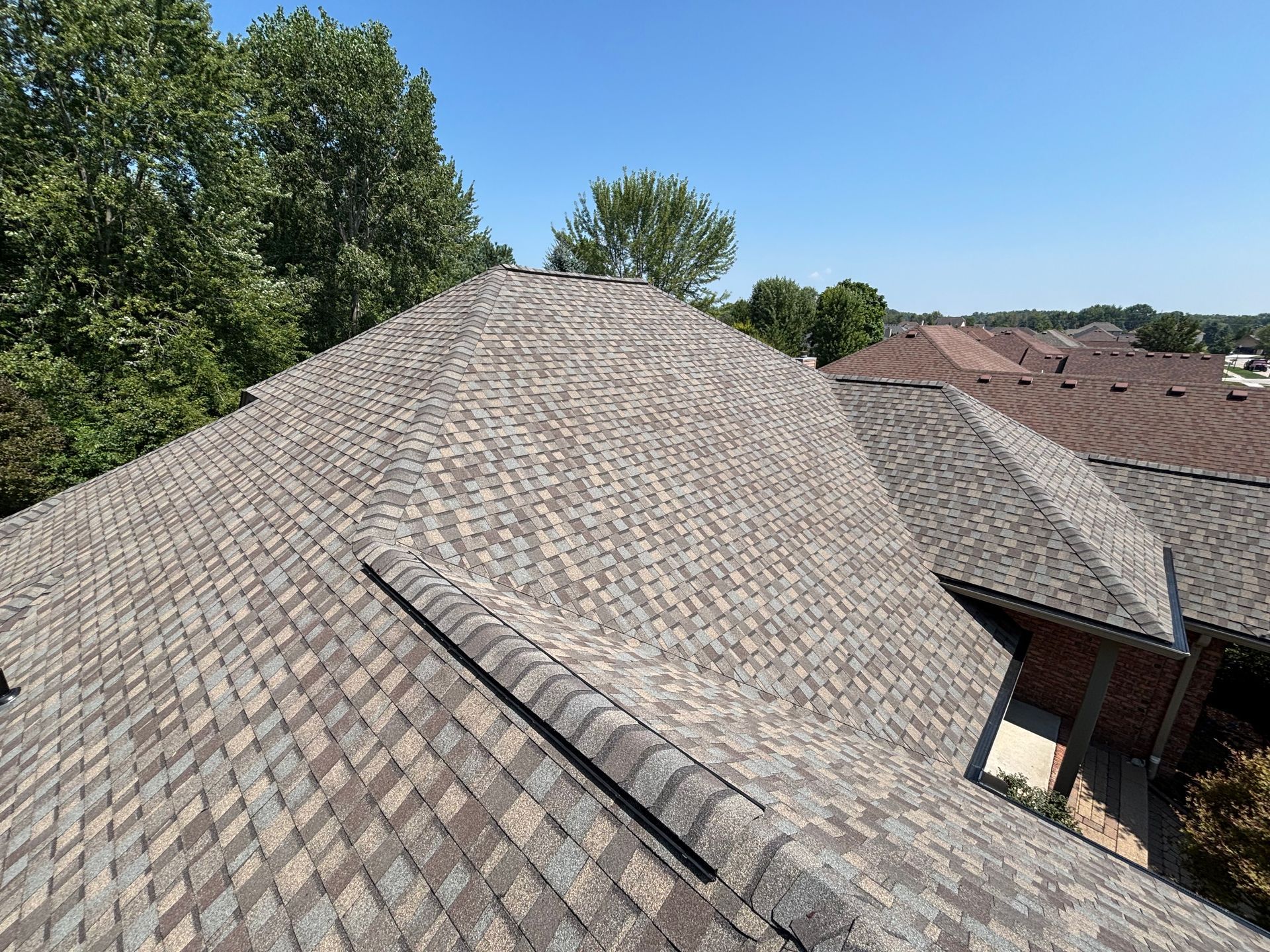 A person wearing a red shirt and tool belt standing on a ladder, installing material on the exterior wall of a building.