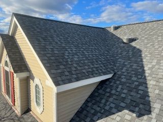 A line of gray pigeons perched on the edge of a rustic roof against a bright blue sky with scattered clouds.