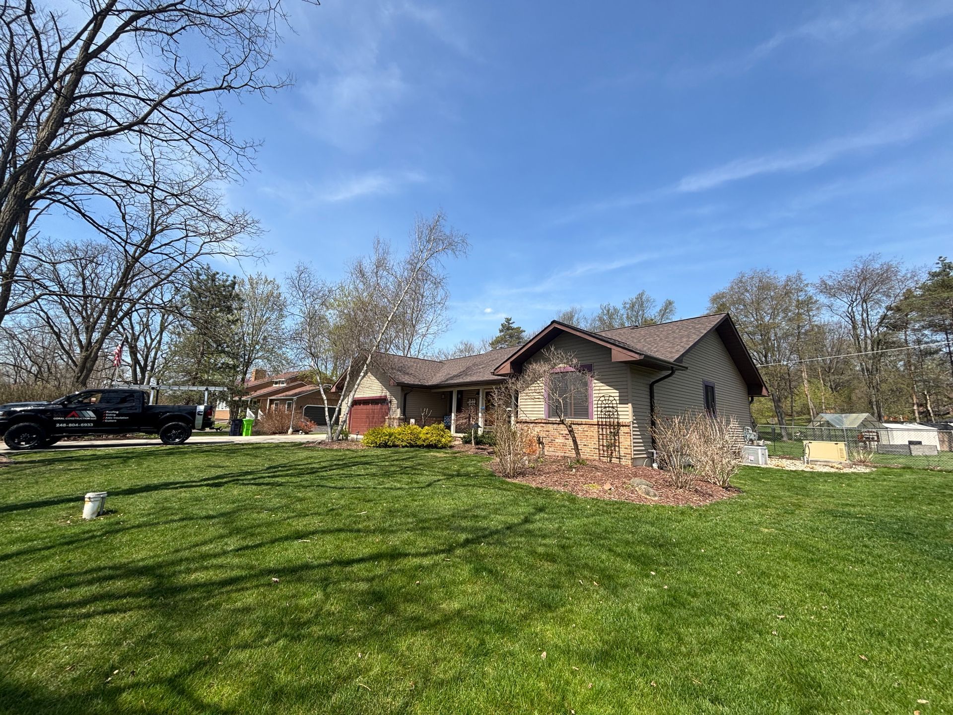 A roofer in a yellow hard hat and high-visibility jacket kneeling on a tiled roof, cleaning leaves with a green bag.