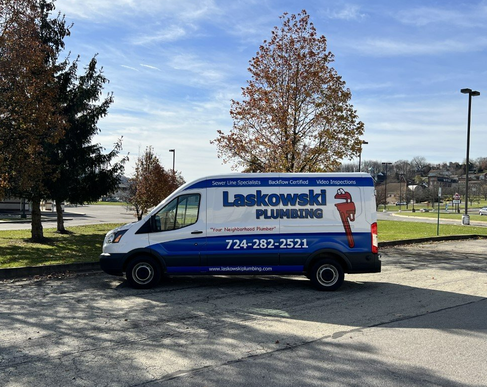 A white and blue Laskowld Plumbing van parked outdoors with a red pipe wrench logo.