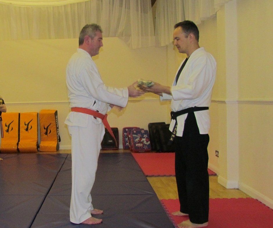 Two men in martial arts uniforms are shaking hands in a gym