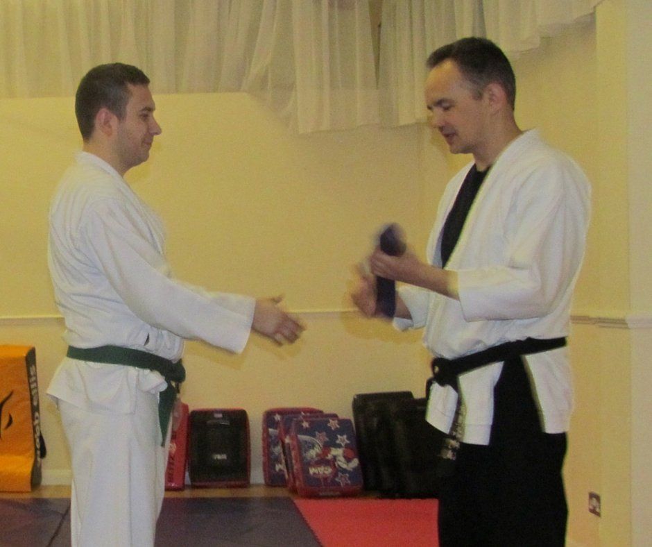 Two men in martial arts uniforms shake hands in a gym