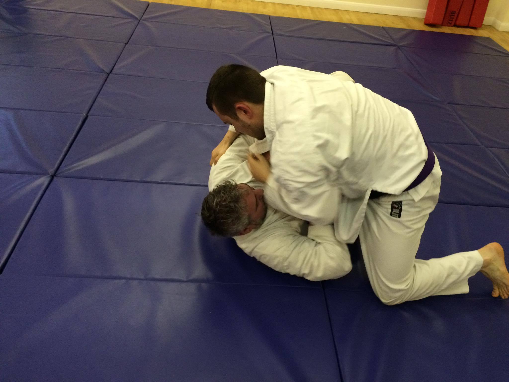 Two men are wrestling on a mat in a gym.