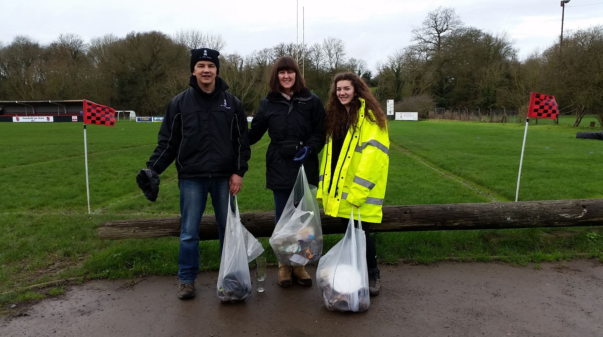 A group of people standing next to each other holding bags of trash.