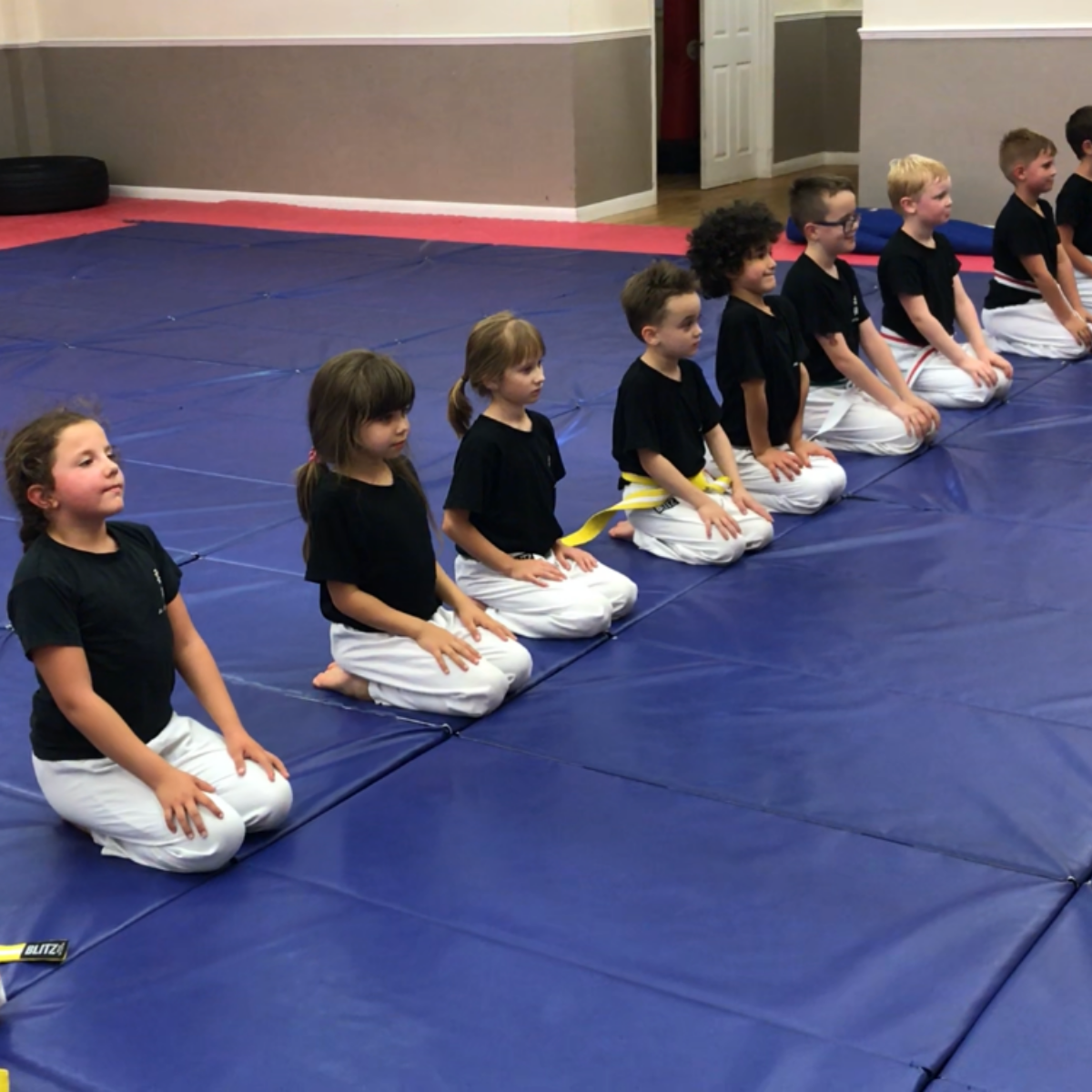 A group of children are sitting on a blue mat