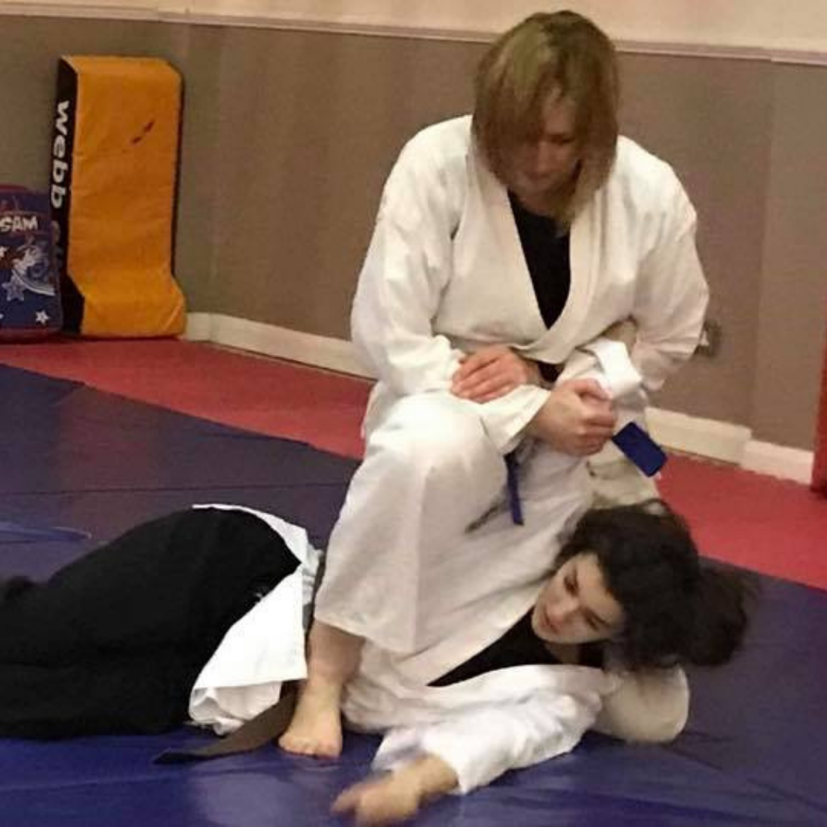 A woman in a white kimono is kneeling over another woman on a mat