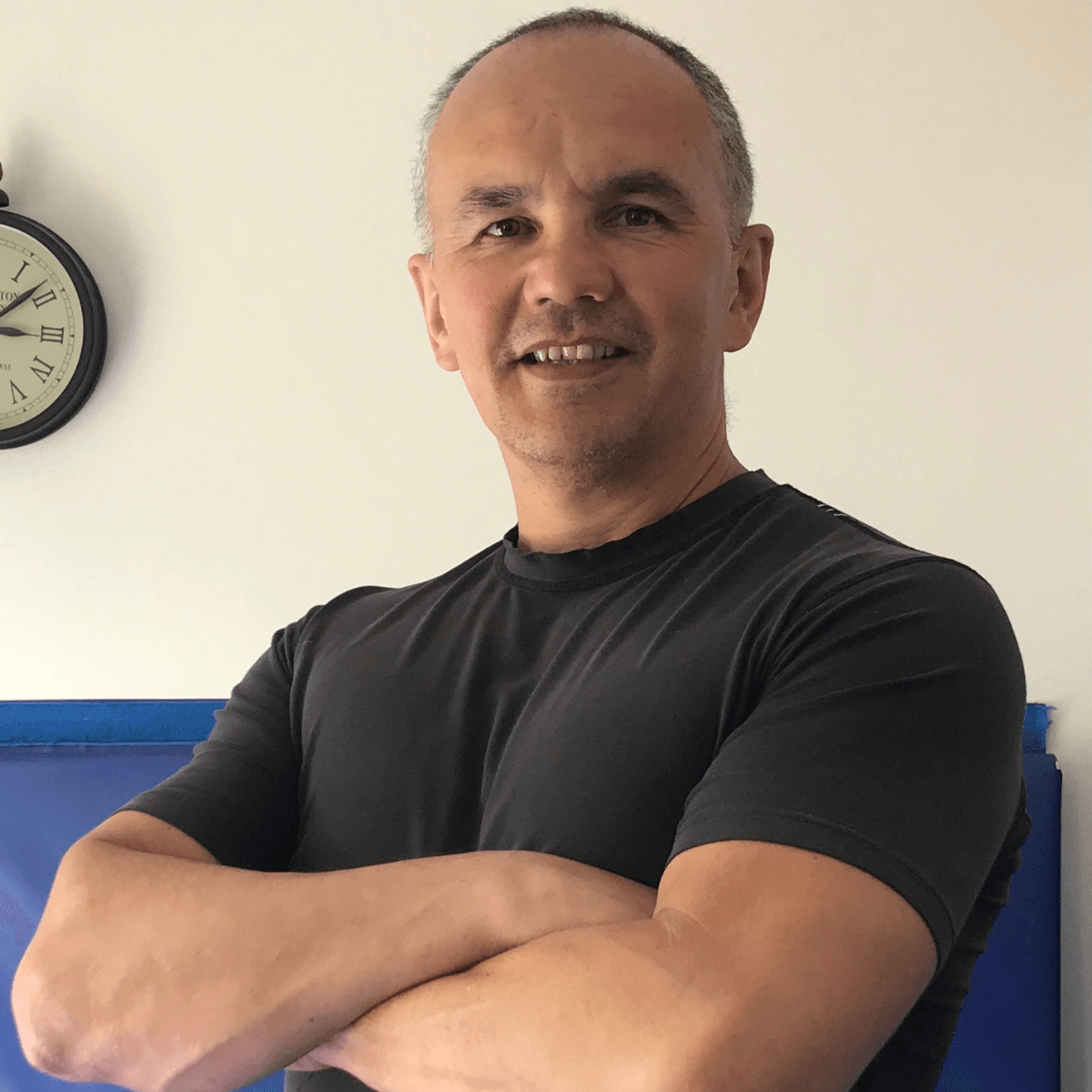 A man with his arms crossed in front of a clock