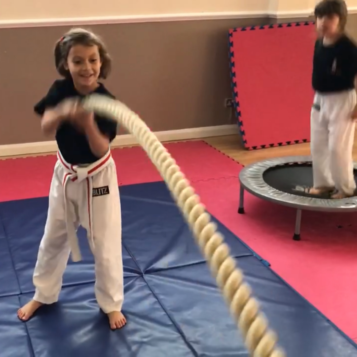 Two young girls are playing with a rope and one has a belt that says karate