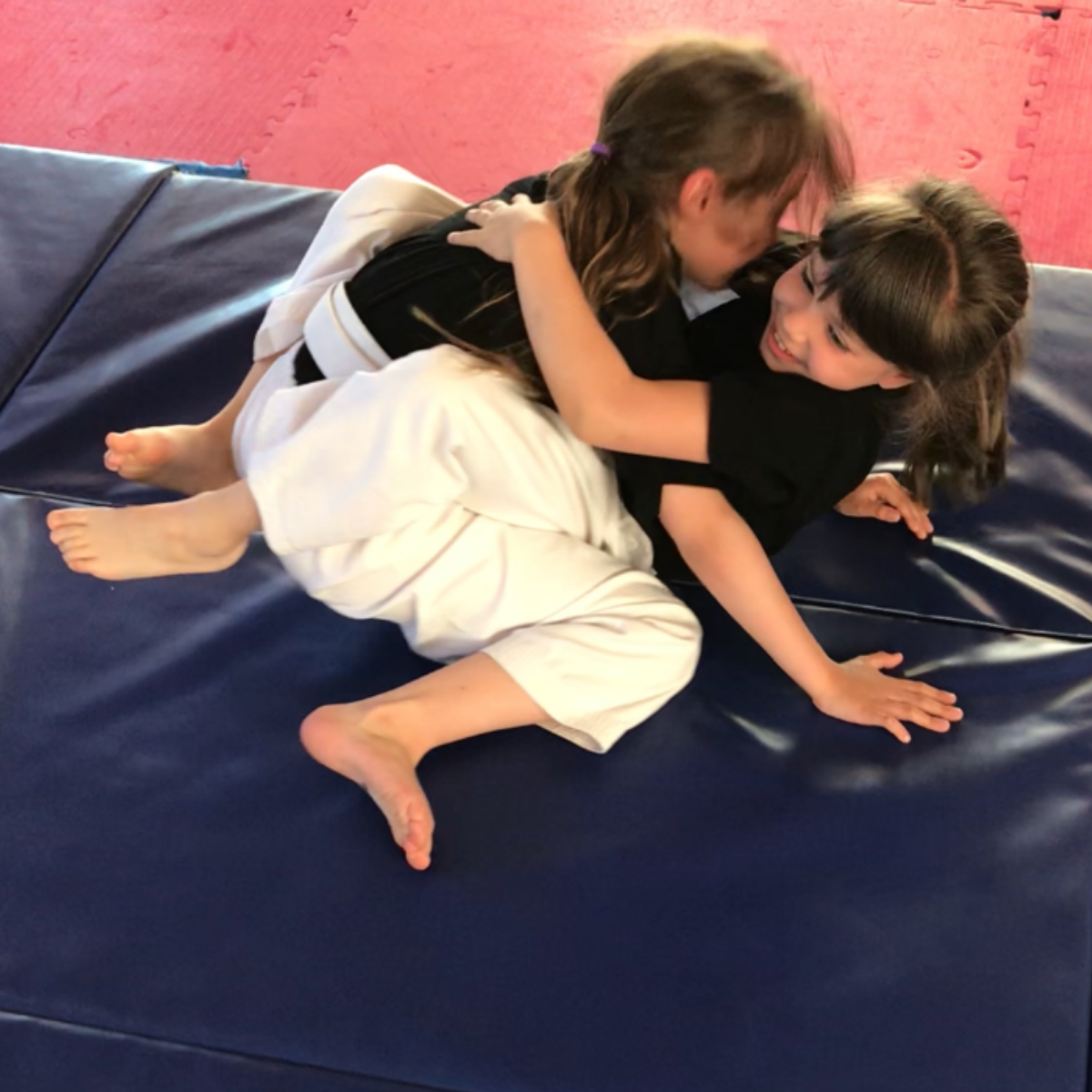 Two little girls are wrestling on a blue mat
