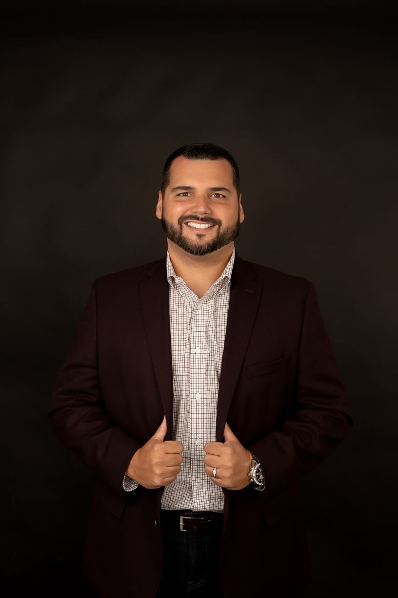 A man in a suit and plaid shirt is standing in front of a black background.