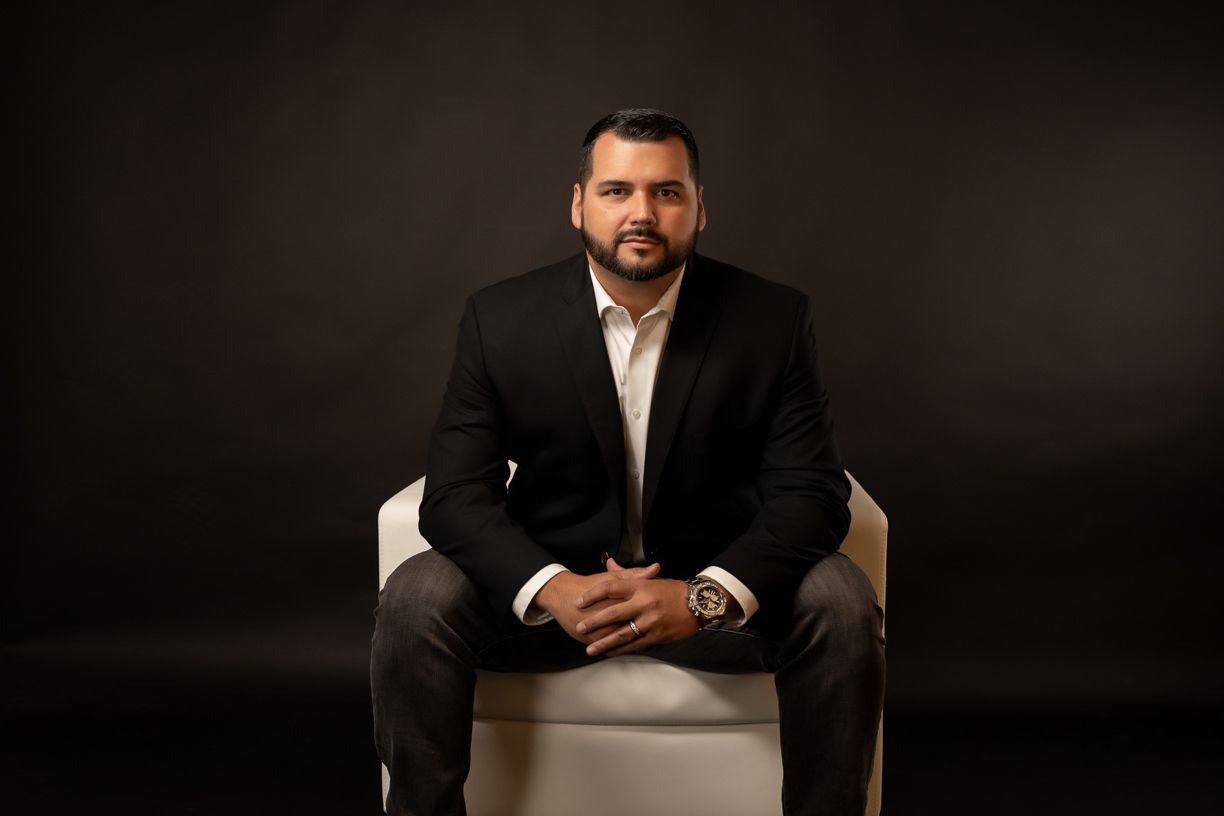 A man in a suit is sitting in a chair with his hands folded.