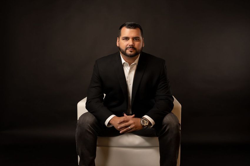 A man in a suit is sitting in a chair with his hands folded.
