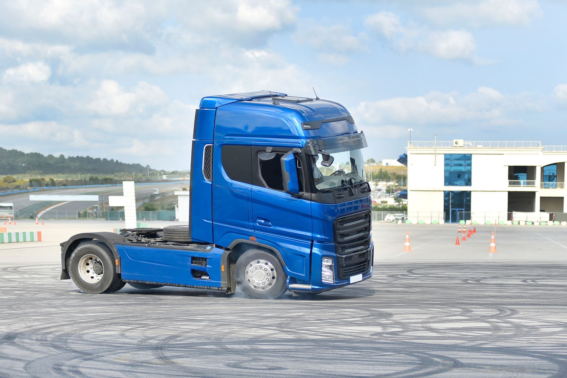 Blue semi-truck driving on a gray surface, possibly a test track, with smoke coming from tires. Blue semi-truck driving on a gray surface, possibly a test track, with smoke coming from tires.