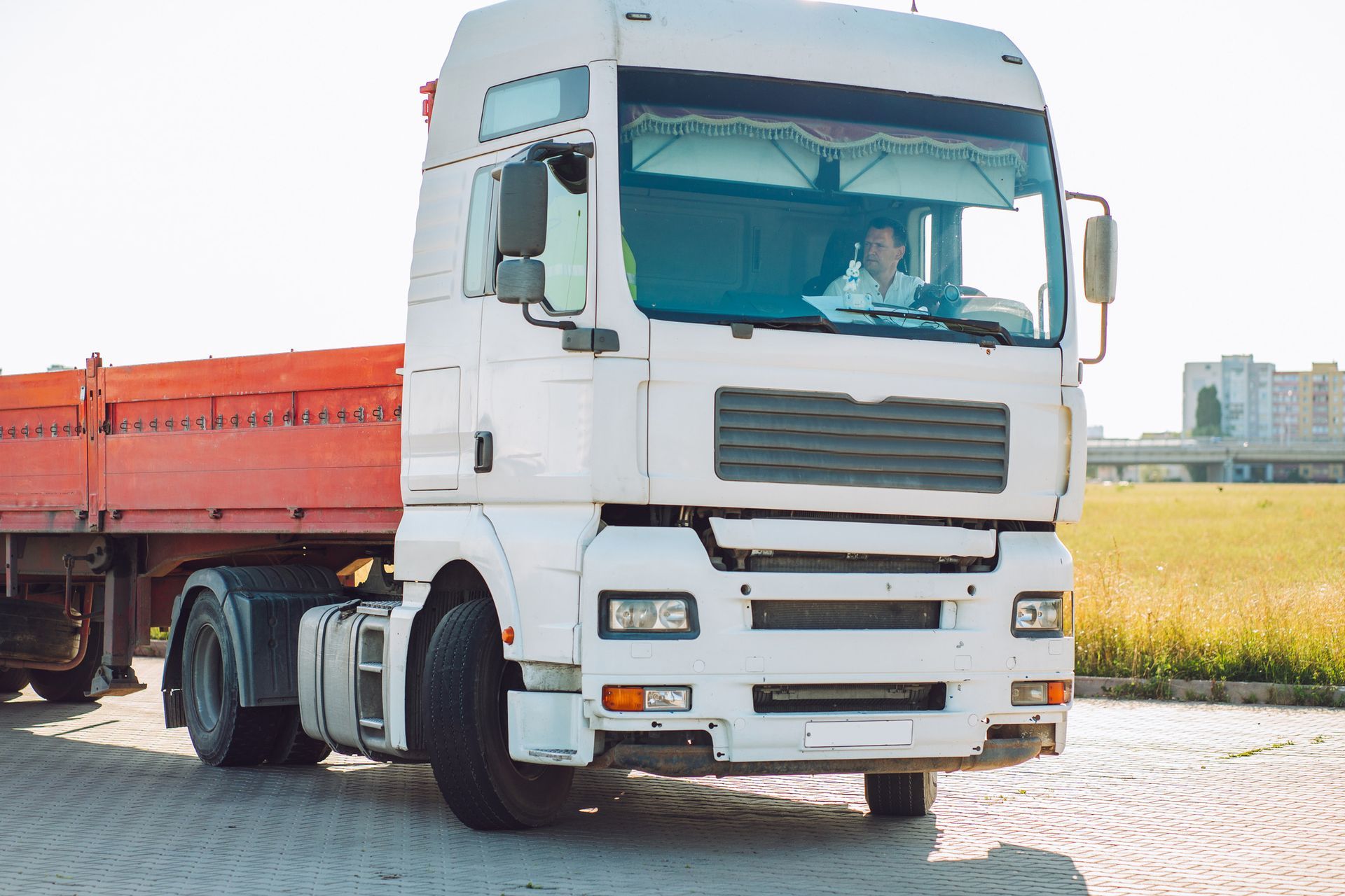 White semi-truck with red trailer, driver visible, on paved road. White semi-truck with red trailer, driver visible, on paved road.