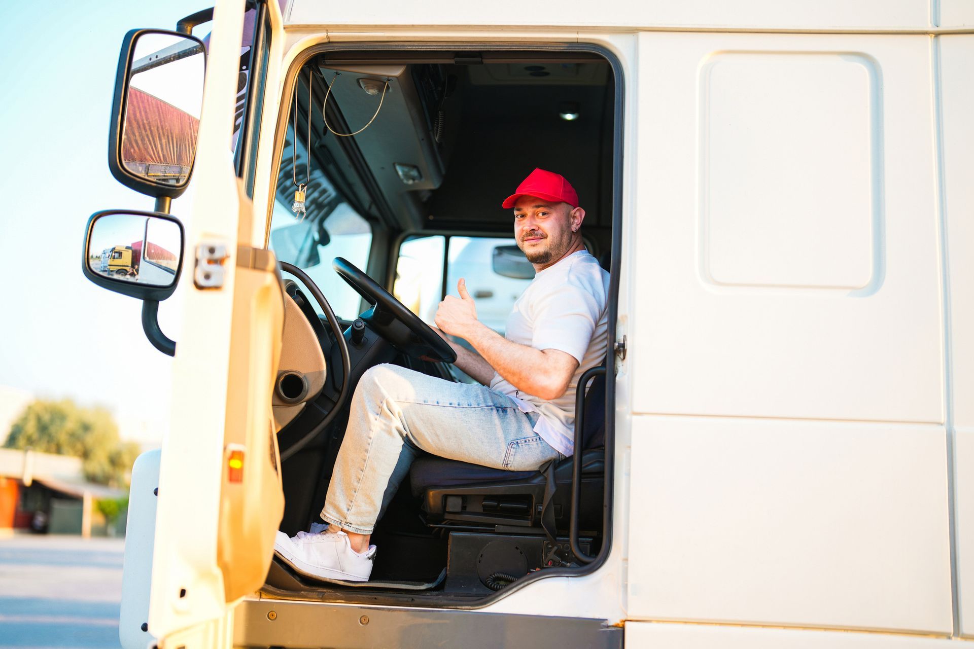 Man in red cap giving thumbs-up, sitting in a truck cab. Sunlight streams in. Man in red cap giving thumbs-up, sitting in a truck cab. Sunlight streams in.