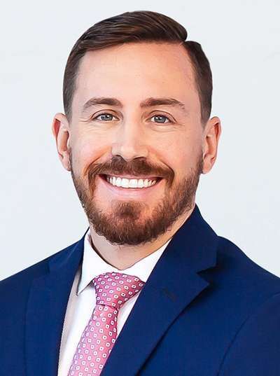 A man in a blue suit and pink tie is smiling for the camera.