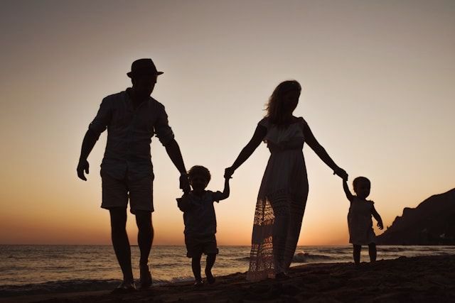 A family is walking on the beach at sunset holding hands.