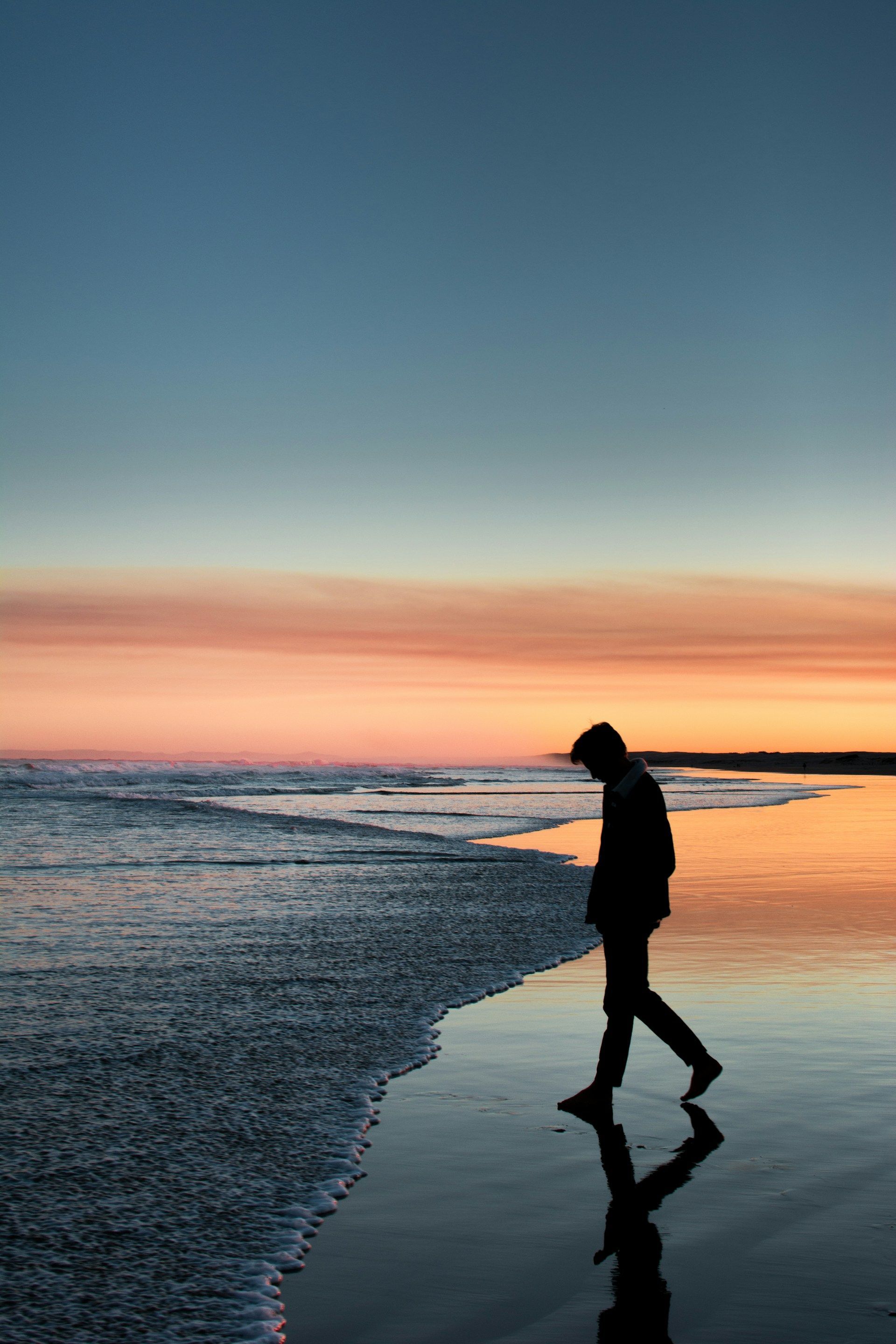 A man is walking on the beach at sunset.