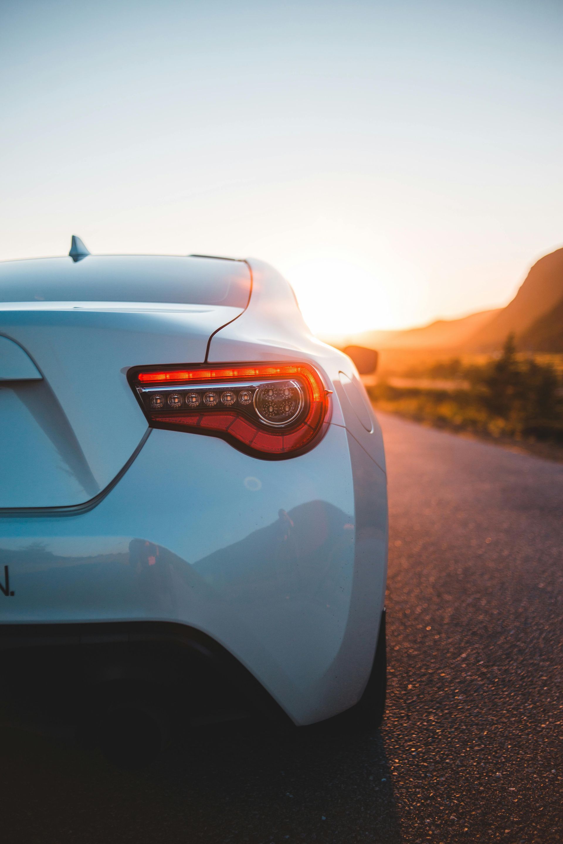 A white car is parked on the side of a road at sunset.