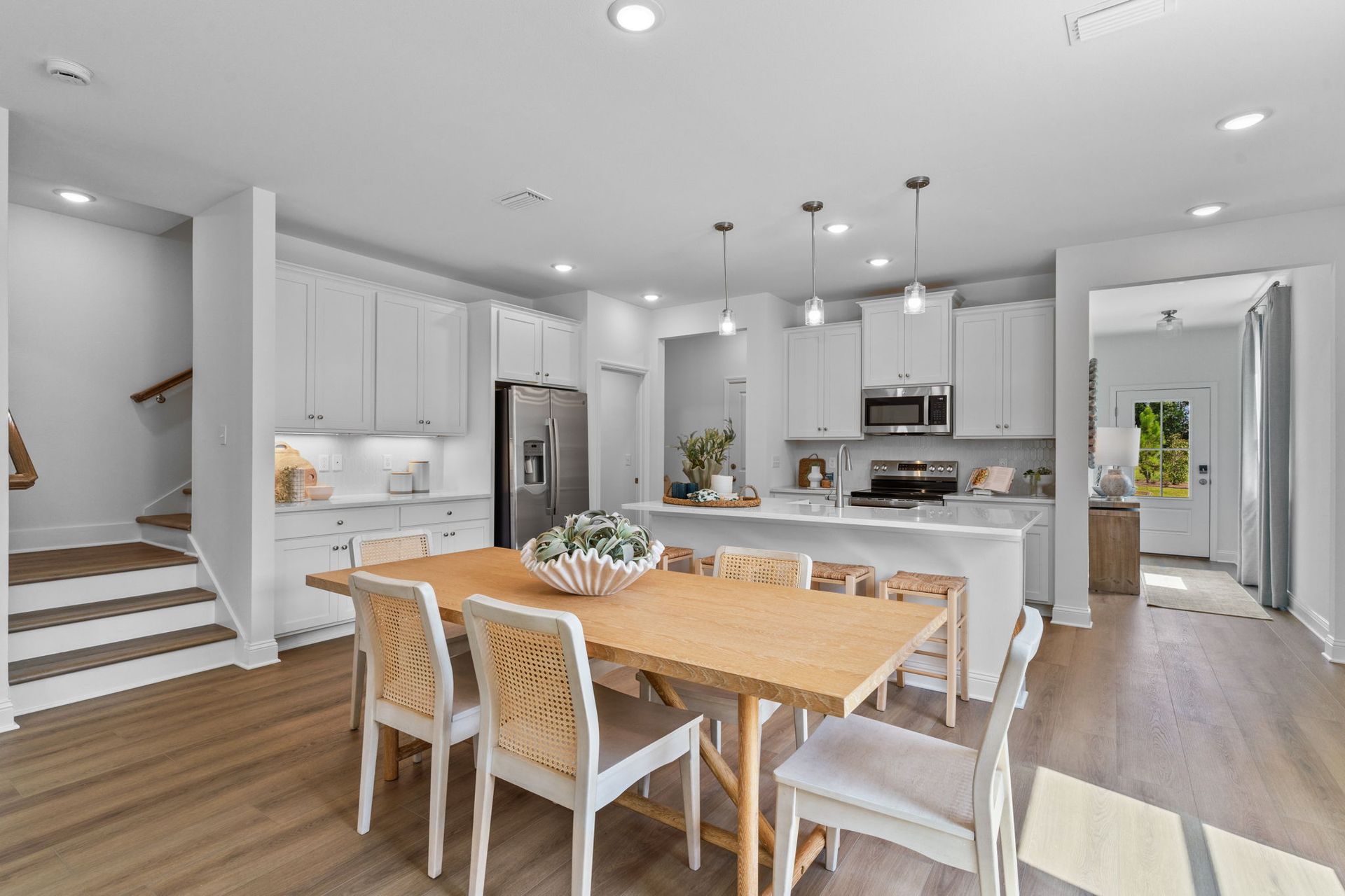Open kitchen and dining area with wood table, white cabinets, and stainless steel appliances.