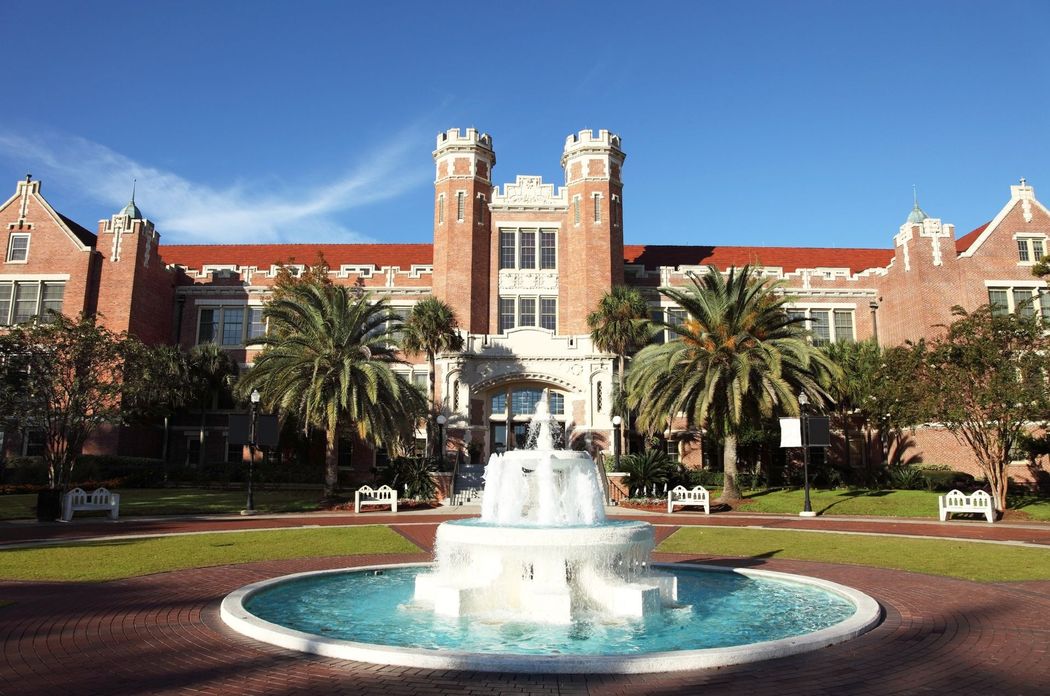 Fountain in front of a brick building with towers, Florida State University campus. Blue sky and palm trees.