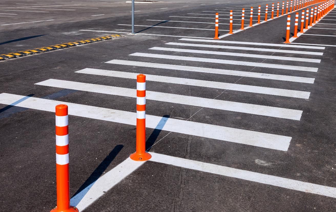 Crosswalk with orange and white bollards on asphalt pavement.