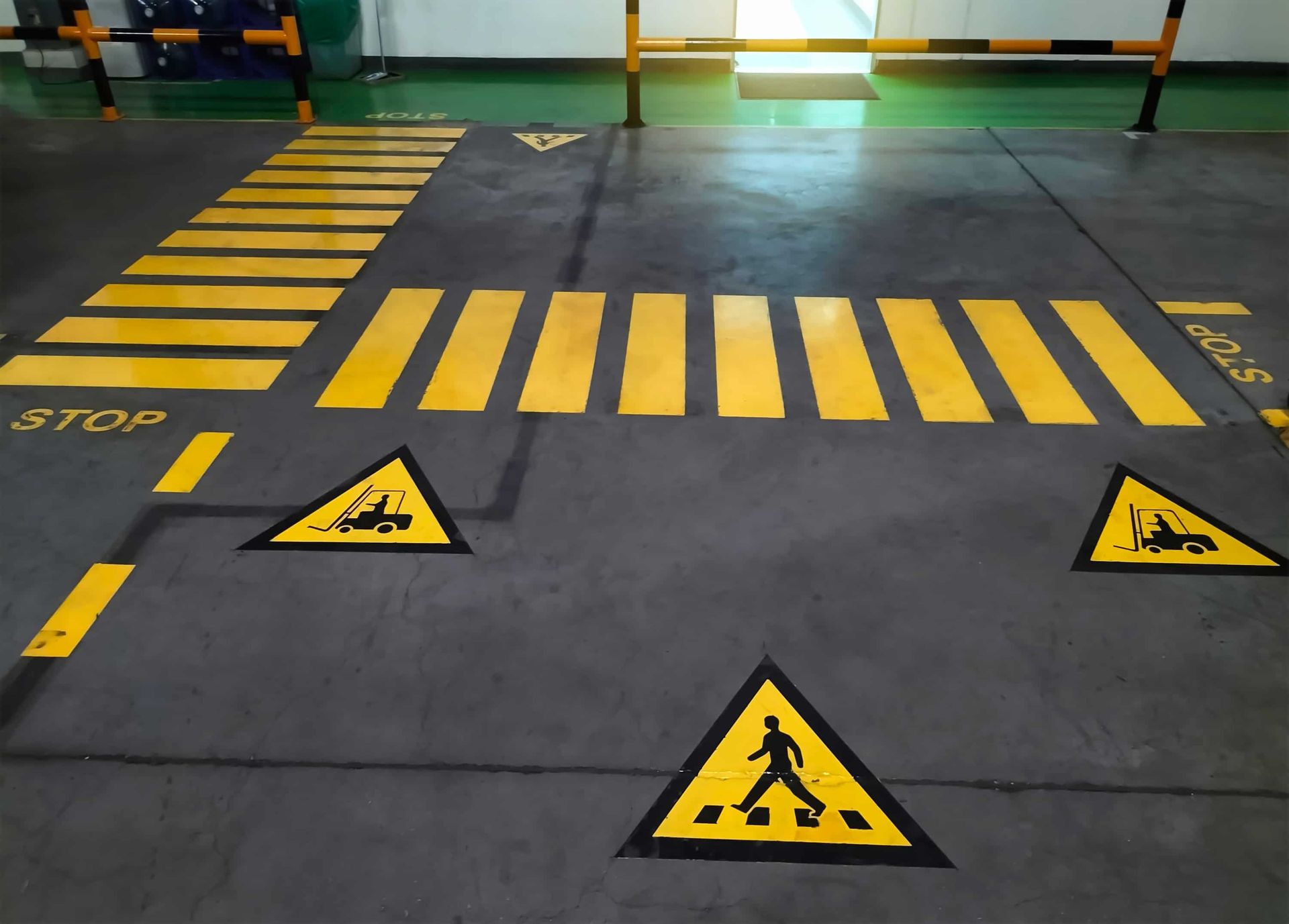 Yellow pedestrian crossings, stop lines, and warning signs on gray floor in a warehouse setting.