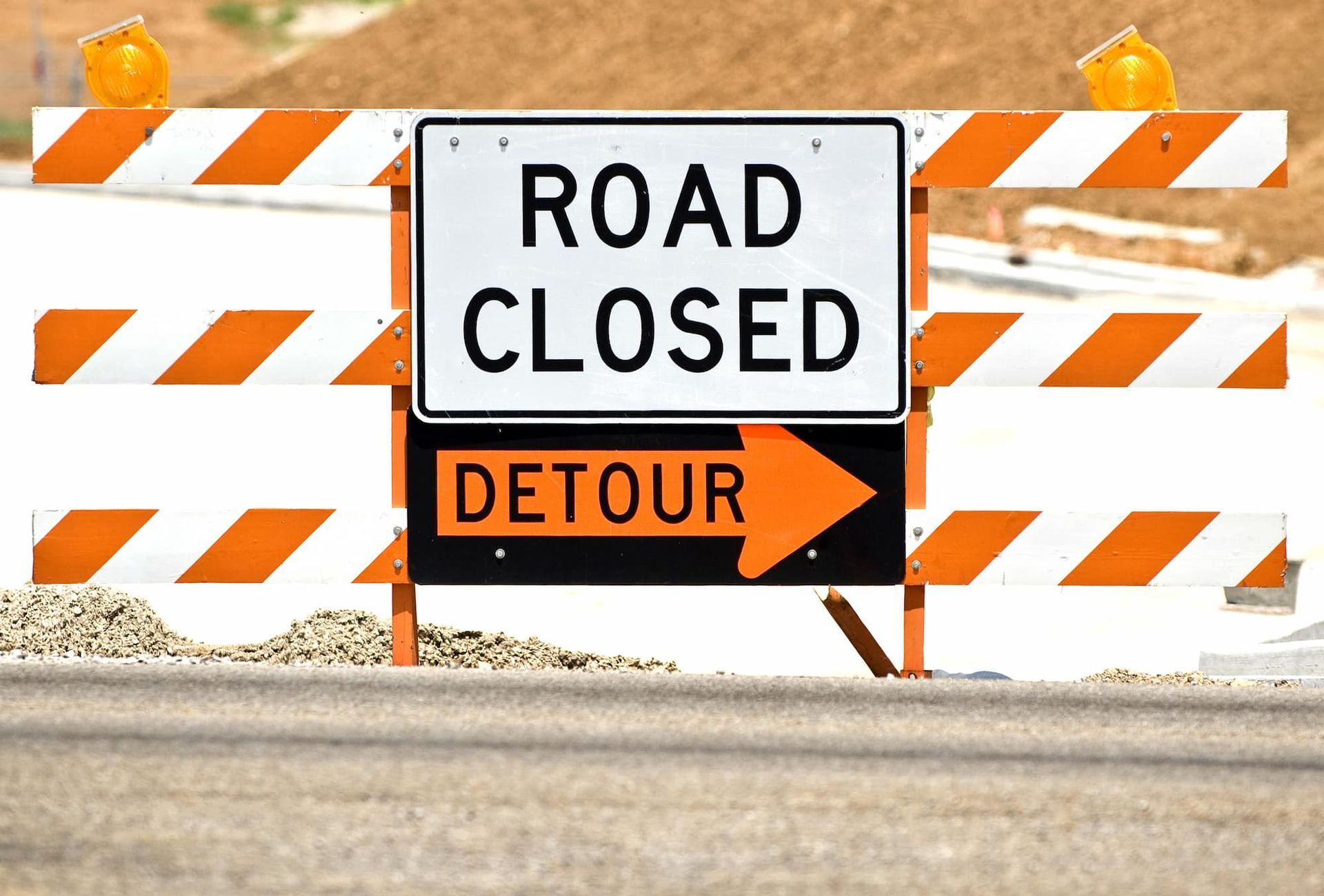 Road closed sign with detour arrow on an orange and white barricade.