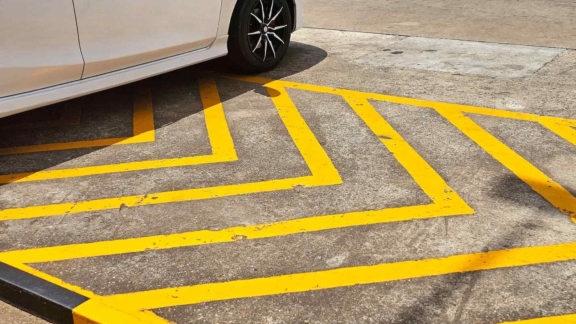 White car parked on a concrete surface with yellow chevron markings.