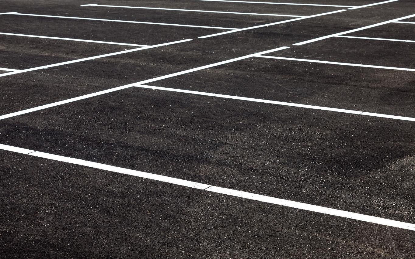Empty asphalt parking lot with white painted parking space lines.