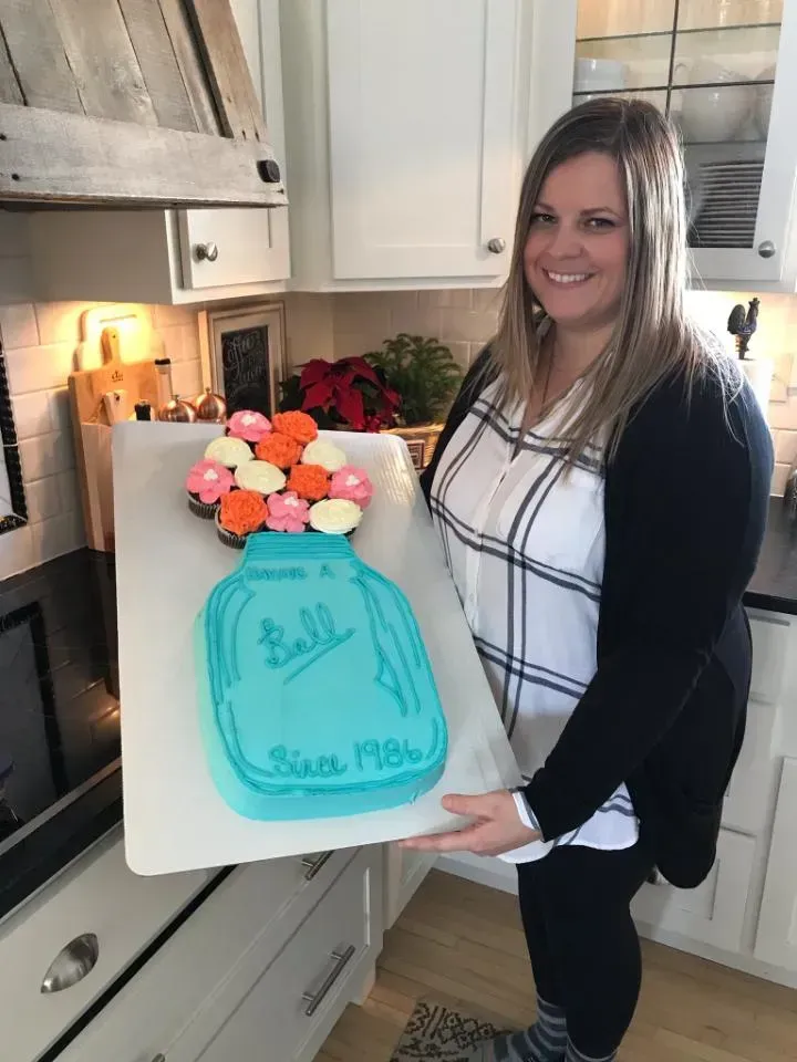 A woman is holding a tray of cupcakes in a kitchen.
